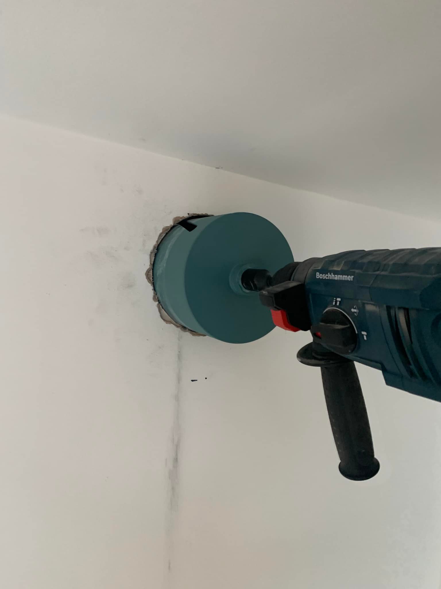Green drill drilling through wall to the outside